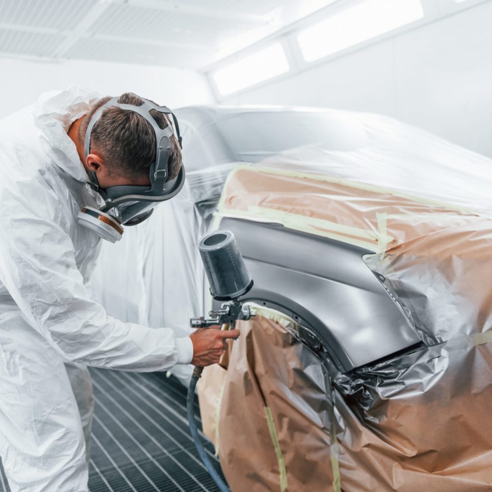 Painting job in progress. Caucasian automobile repairman in uniform works in garage.